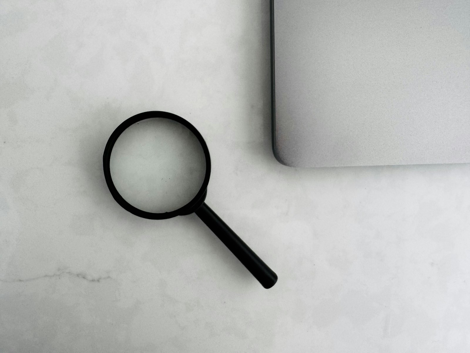 Magnifying glass beside a closed laptop, the close reading a prep platform's advertised pass rate and its disclosure both require